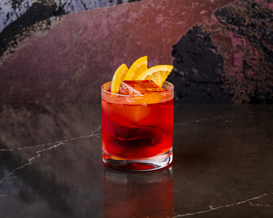 A Boulevardier cocktail served over ice in a rocks glass, garnished with an orange peel.