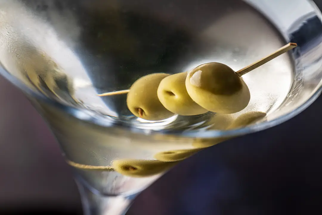 Close-up of a classic Martini in a cocktail glass, garnished with three green olives on a pick