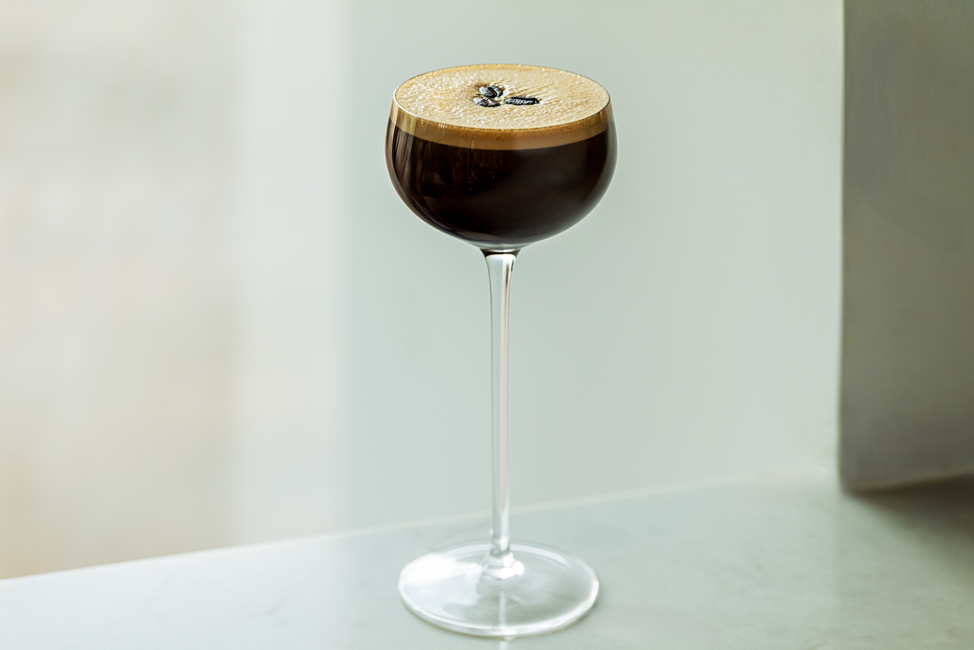 An Espresso Martini cocktail served up in a coupe glass with a foamy top, garnished with coffee beans.