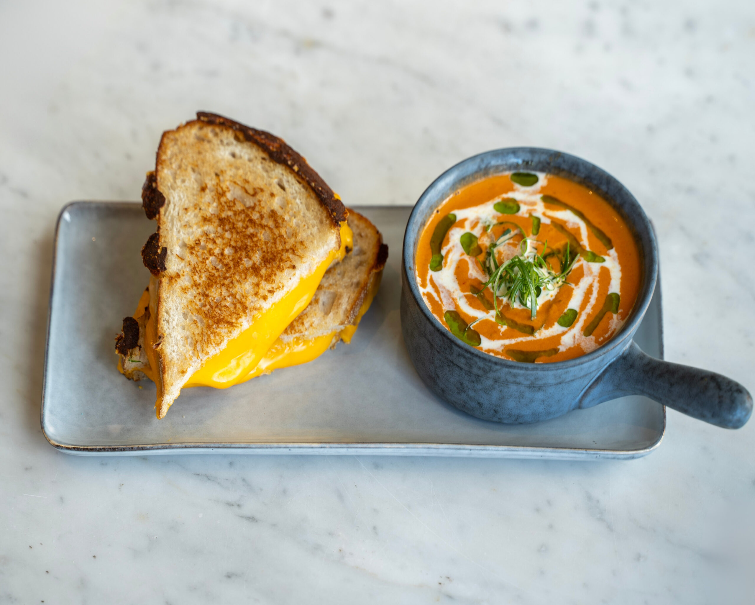 Close-up of a golden brown grilled cheese sandwich with a side of creamy tomato basil soup for dipping.