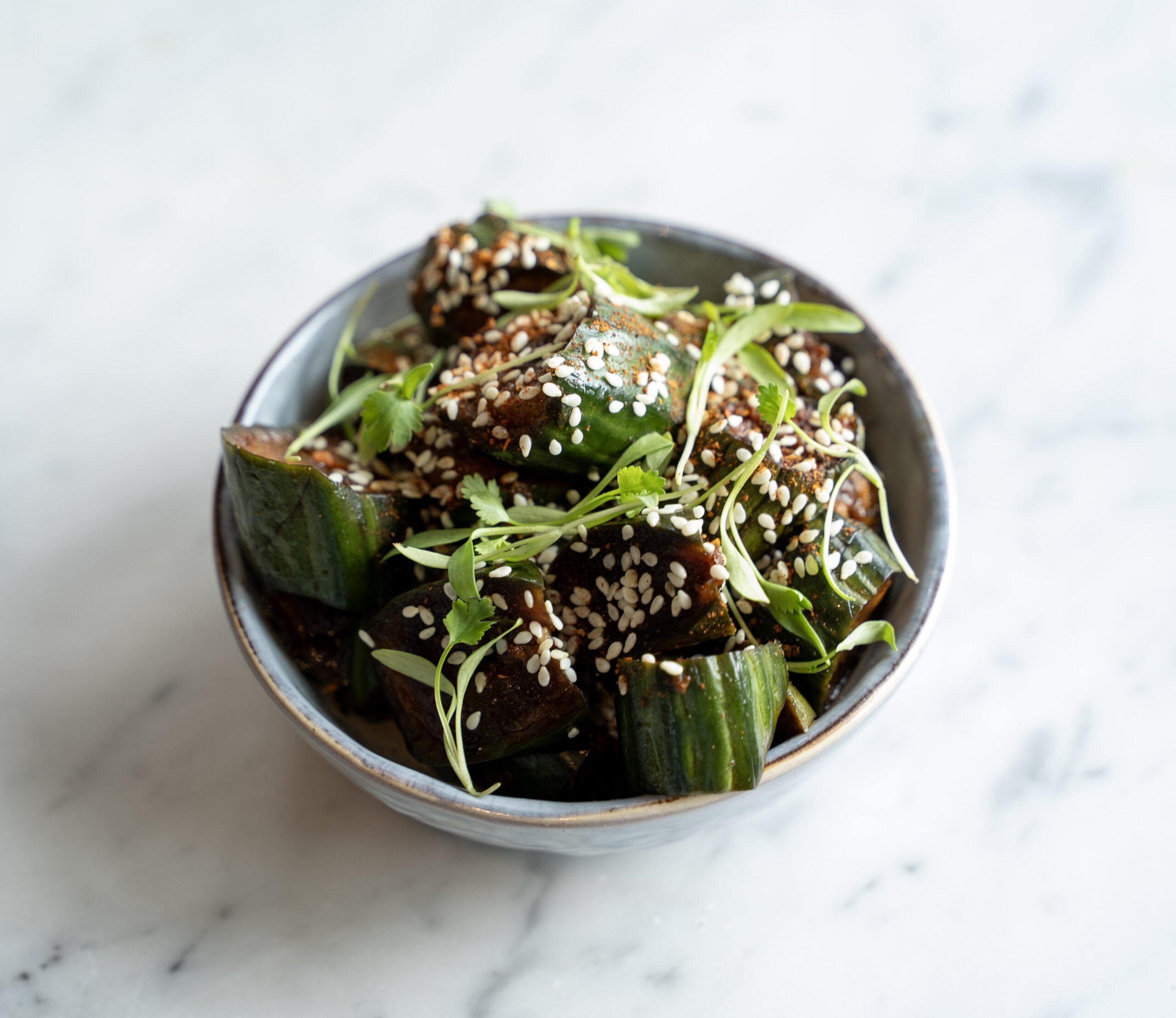 Chili crisp cucumber salad with sesame seeds and herbs in a ceramic bowl