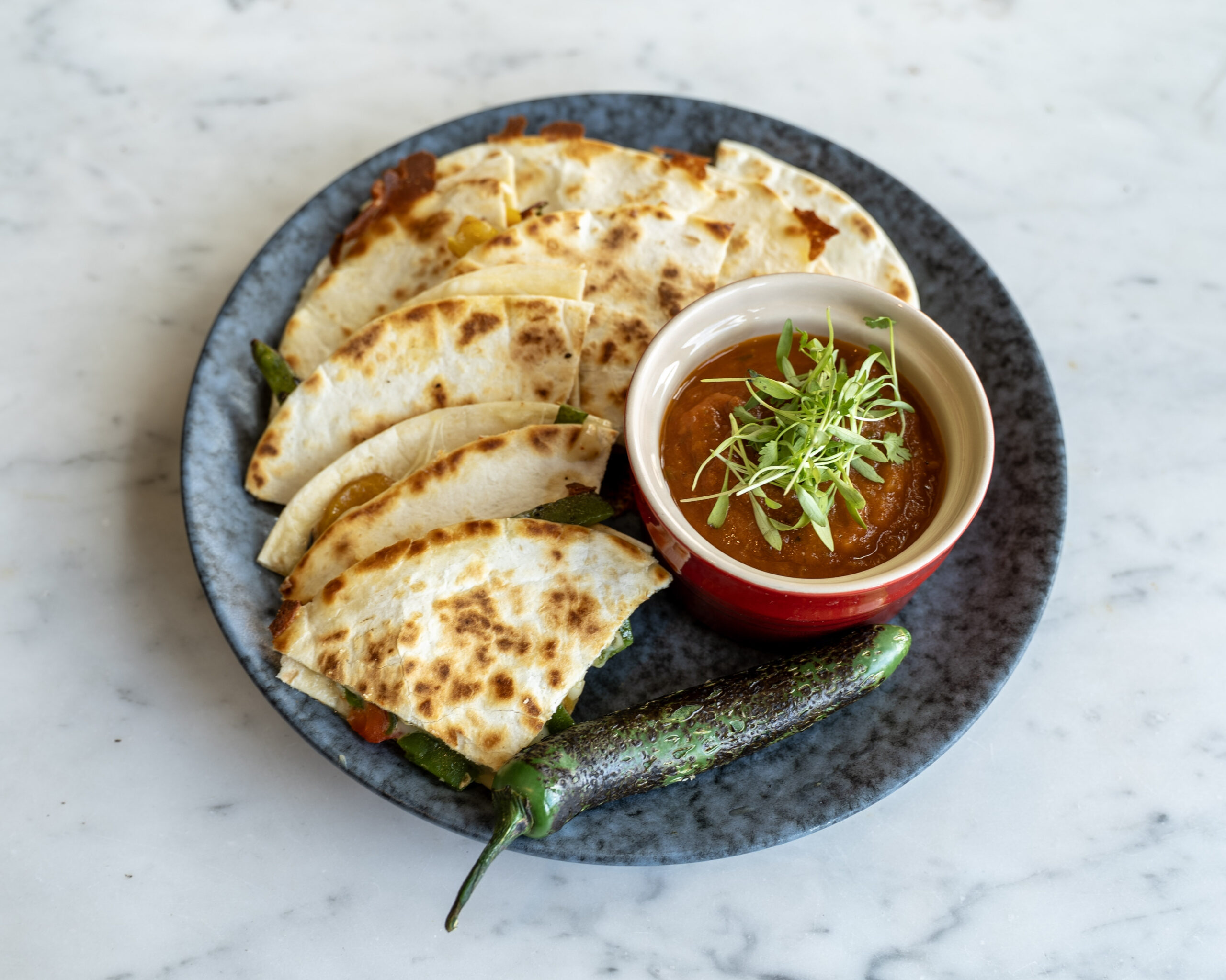 Roasted pepper quesadilla on a plate with cilantro and a small bowl of salsa